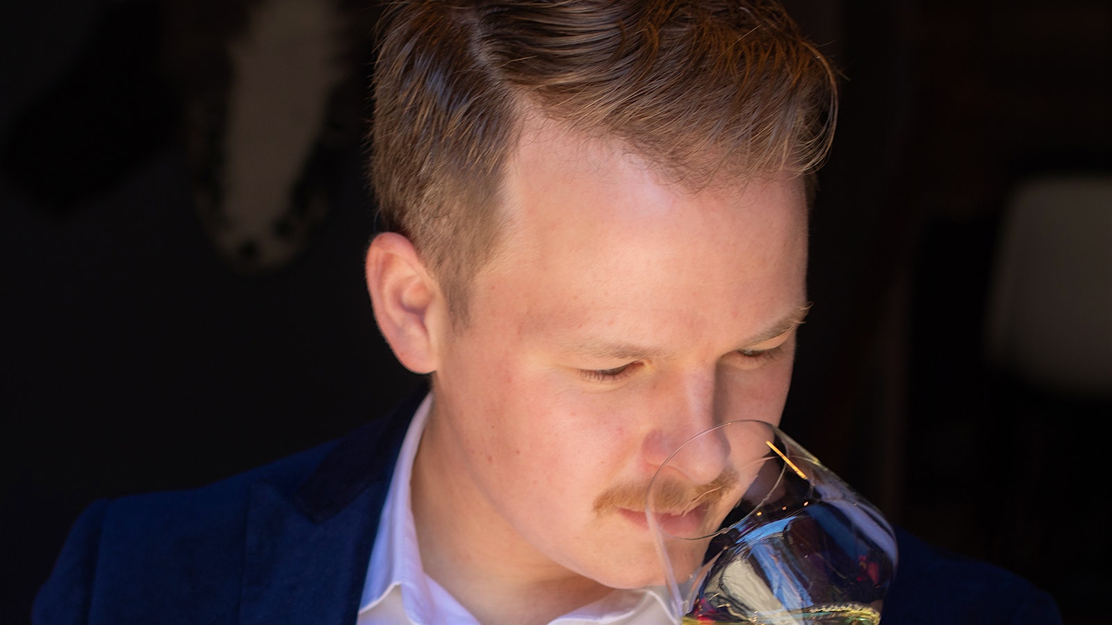 A portrait of Jacob Brown, sniffing a wine glass.